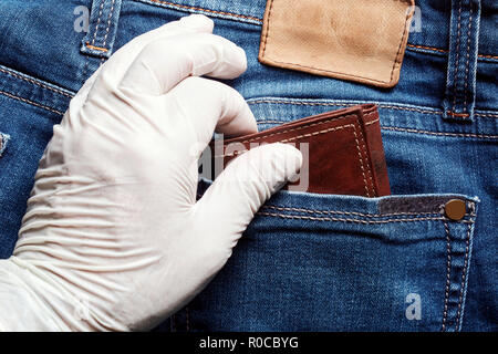 Thief wearing a white vinyl glove steals a wallet from the back pocket of jeans. Close up view of pickpocketing. Stock Photo