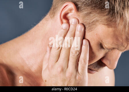 Man has a sore ear. Man suffering from otitis on blue background Stock Photo