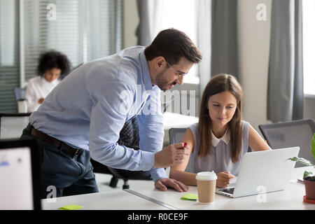 Middle aged mentor explaining online work to young focused inter Stock Photo