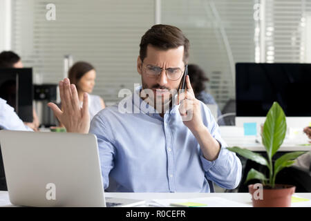 Angry businessman caller talking on phone disputing over compute Stock Photo