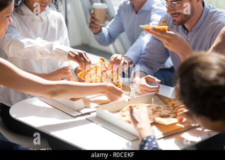 Diverse workers taking pizza from box on table eating together Stock Photo