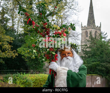 UK, Market Bosworth, Victorian Christmas Fair - December 2015: Father Christmas robed in green, masked and carrying holly branches, church tower in ba Stock Photo