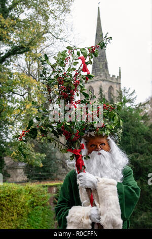 UK, Market Bosworth, Victorian Christmas Fair - December 2015: Father Christmas robed in green, masked and carrying holly branches, church tower in ba Stock Photo