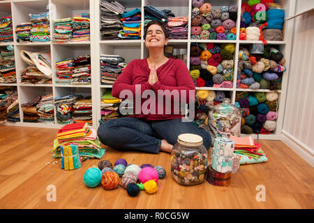 Person sits in a meditative position in their craft sewing space surrounded by creative colour Stock Photo