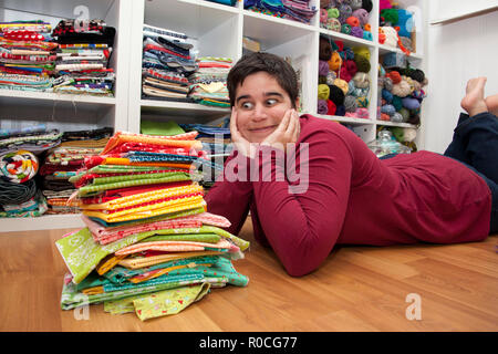 Person laying in front of a stack of colorful fabric looking wide eyed and excited Stock Photo