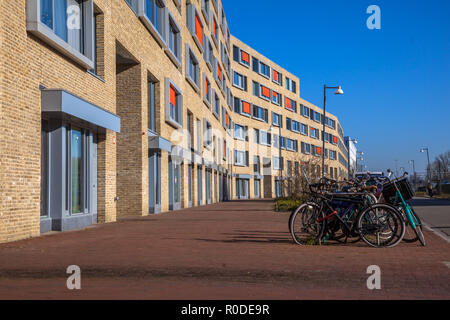Modern apartment block with light bricks and orange sun screens in a suburban neighbourhood with bicycles parked in front Stock Photo