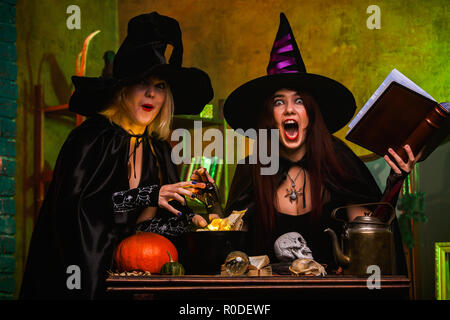 Image of two smiling two witches in black hats reading book of incantations Stock Photo