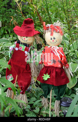 Two scarecrows in festive outfits guarding a flower bed. Stock Photo