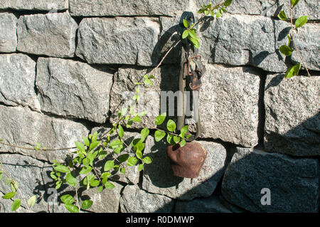 Old used weathered grunge cowbell hanging on solid stone wall closeup in sunny day Stock Photo