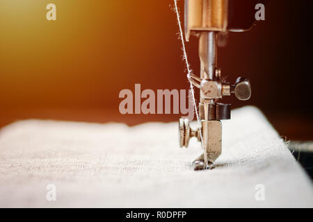Part of vintage hand sewing machine and item of clothing. Steel needle with looper and presser foot close-up. Stock Photo