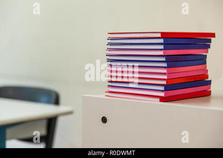 Stack of Multicolored Notebooks on a Drawer with School Furniture in Background Stock Photo