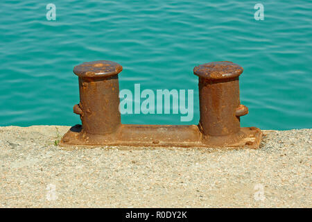 Steel rusty dual mooring bitt on a fragment of old concrete pier on the background turquoise sea water in calm Stock Photo