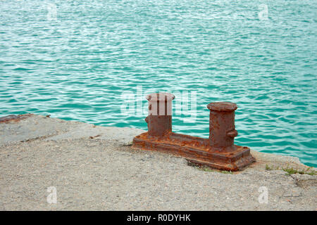 Steel rusty dual mooring bitt on a fragment of old concrete pier on the background turquoise sea water Stock Photo