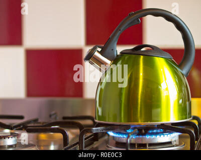 green kettle on a modern stove in front of a red with white wall Stock Photo