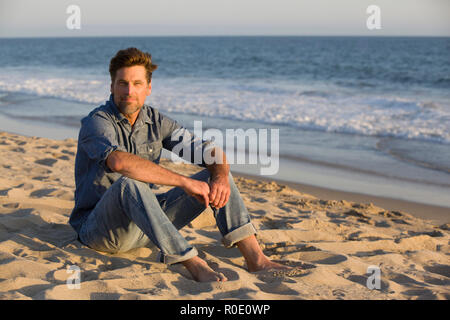 Mid-Adult Man Sitting on Sandy Beach Stock Photo