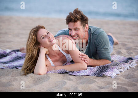 Smiling Mid-Adult Couple Laying on Blanket at Beach Stock Photo