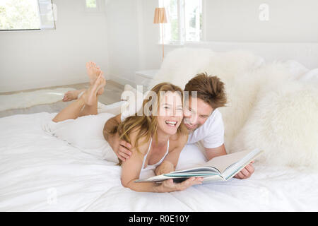 Playful Mid-Adult Couple Looking at Book on Bed Stock Photo