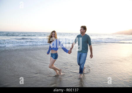 Romantic Mid-Adult Couple Holding Hands While Walking Along Beach Stock Photo