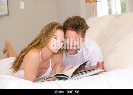 Smiling Mid-Adult Couple Reading Book on Bed Stock Photo