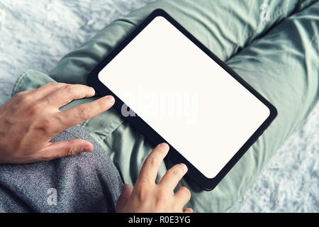 Top-down shot of a long sitting man with a digital tablet on his legs. Man on a sofa starts working on an empty screened tablet. Man slightly touches  Stock Photo