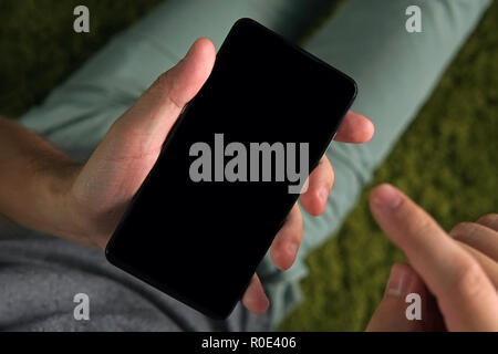 Close up of a young man using the smartphone with the white screen. Person is on-line from a smartphone. Man holds a phone and raises the right index  Stock Photo