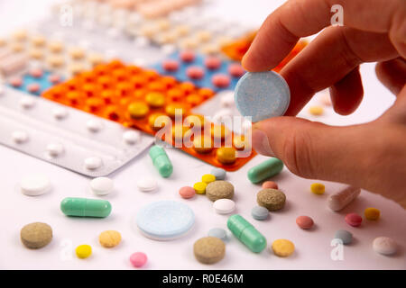 Male hand holds blue pill above colorful pills and capsules in plastic packs - blisters. Global pharmaceutical industry for billions dollars per year. Stock Photo