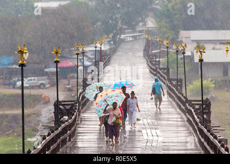 SANGHLABURI, THAILAND, JANUARY 24, 2016 : Thai family is walking under a heavy rain on the Mon bridge in Sanghlaburi, Thailand Stock Photo