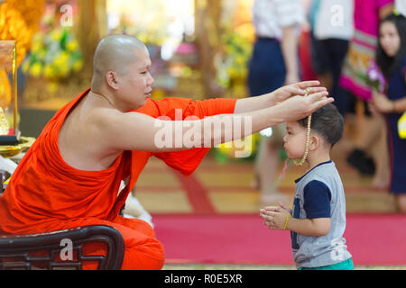 SANGKHLABURI, THAILAND, JANUARY 24, 2016 :  A buddhist monk is blessing a little boy  by inserting a rosary necklace around his neck in the Wat Wang W Stock Photo