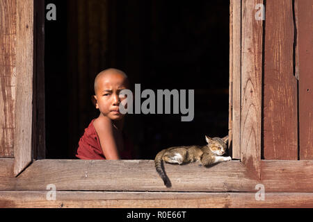 NYAUNG SHWE, MYANMAR, JANUARY 27, 2015 : A young novice buddhist monk is looking at the window of the Shwe Yaunghwe Kyaung monastery in Nyaung Shwe, M Stock Photo