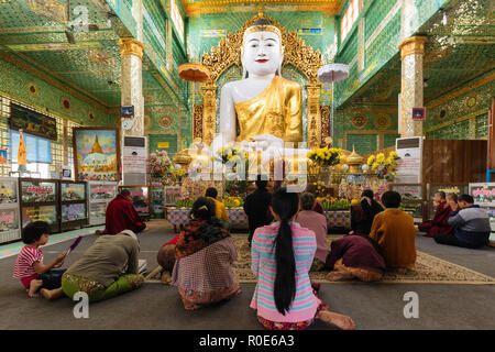 SAGAING, MYANMAR, JANUARY 16, 2015 : People are sitting on the floor for praying the large golden Buddha in the Soon U Ponya Shin Paya pagoda, Sagaing Stock Photo