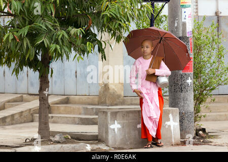 MANDALAY,MYANMAR,JANUARY 17, 2015 : A young Buddhist nuns is standing with her umbrella in the streets of Mandalay, Myanmar (Burma). Stock Photo