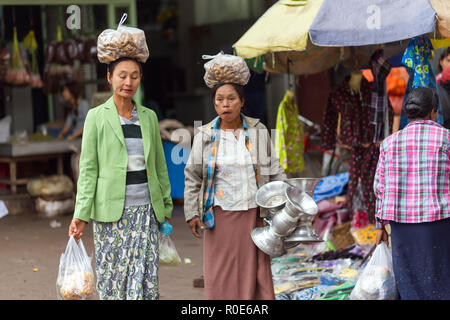 AMARAPURA, MYANMAR, JANUARY 17, 2015 : Two women are carrying bags with galangal roots on their heads, walking in the street of the Zegyo market, in M Stock Photo