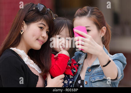 MANDALAY,MYANMAR,JANUARY 16, 2015 : Korean women are shooting a selfie  (self portrait) with a funny bored little girl in a street of Mandalay,  Myanmar Stock Photo - Alamy