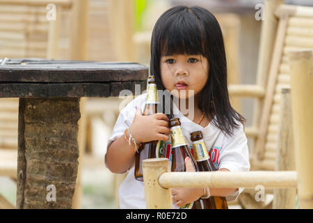 KO PHANGAN, THAILAND, FEBRUARY 21, 2011 : A little girl is holding three beers bottles for clearing the table of her parent's restaurant in the Ko Pha Stock Photo