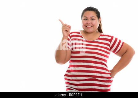 Studio shot of young happy fat Asian woman smiling while pointin Stock Photo