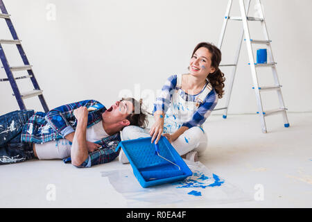 Smiling loving couple doing home renovations. Young woman is holding a paint roller and young man is resting Stock Photo