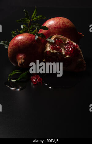 Red pomegranate with grean leaves, reflections in the water and berry surrounded a black nuance Stock Photo
