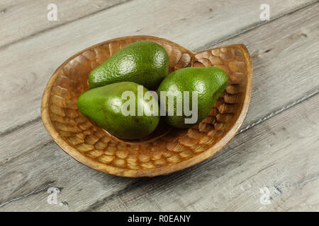 Three whole green avocados on wooden carved bowl. Stock Photo