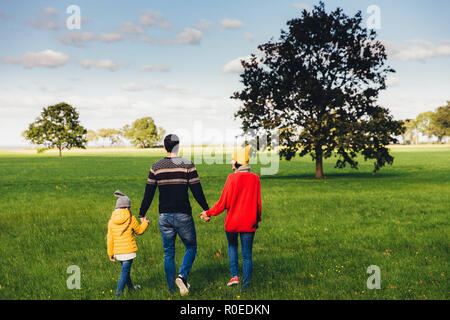 Three friendly family members have walk together on green meadow, keep hands, have pleasant conversation, enjoy togetherness and beautiful landscapes, Stock Photo