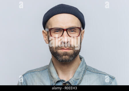 Photo of intelligent confident stylish man with dark thick beard and mustache, looks seriously into camera, poses against grey studio background, wear Stock Photo