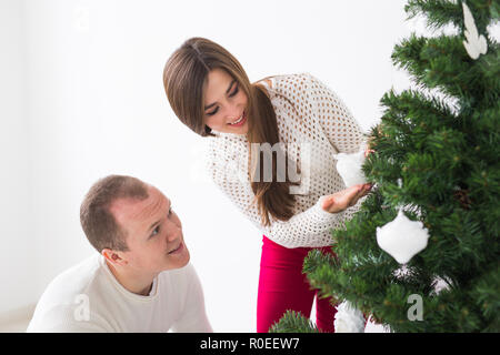 Winter holidays and people concept - Loving couple hanging decorations on Christmas tree Stock Photo