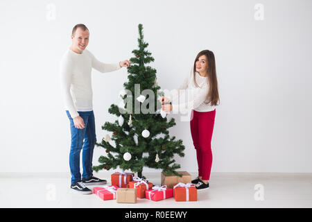 Winter holidays and people concept - Loving couple hanging decorations on Christmas tree Stock Photo