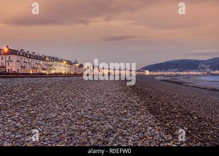 A view of Llandudno’s curving shoreline lined by white fronted hotels at  sunrise. The Great Orme headland is in the distance and a dawn sky is above. Stock Photo