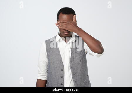 African man in white shirt and vest covering his face with hands Stock Photo