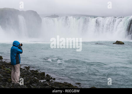 Photographer in blue jacket taking picture of Godafoss waterfall, Iceland. Stock Photo