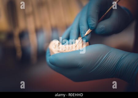 Detailed close up of dental instrument working on a denture or teeth, blue rubber glove, dentistry Stock Photo