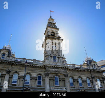 The clock tower on an old stone building in the city of Dunedin is lit up in the sunlight Stock Photo