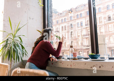 Woman wearing jeans and sweater eating tasty breakfast in cafeteria Stock Photo