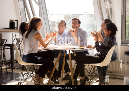Friendly happy diverse workers laughing eating pizza together in Stock Photo
