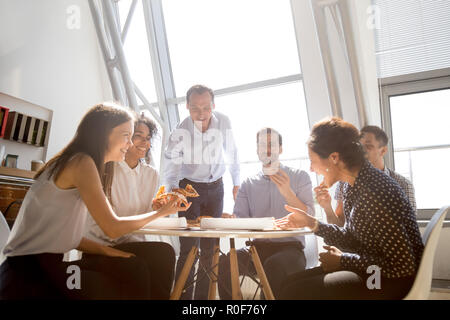 Cheerful diverse team people laughing at joke eating pizza toget Stock Photo